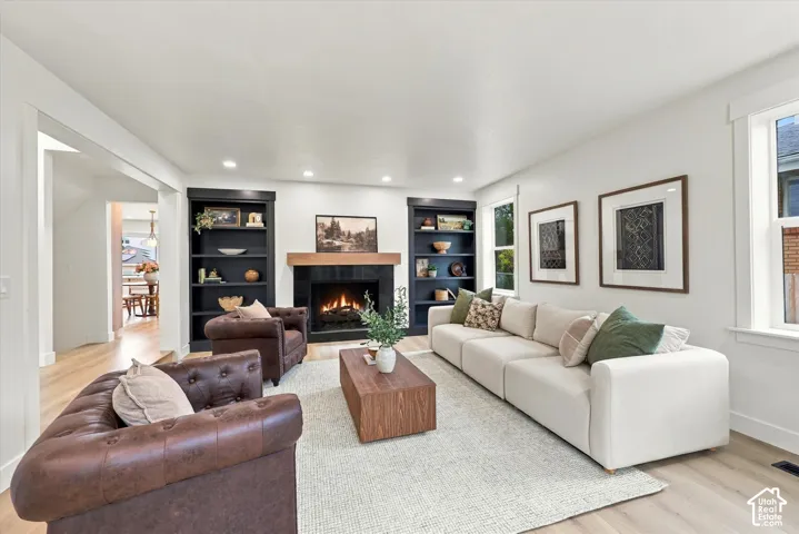 Living area featuring a fireplace with a wood mantle, built-in shelving, recessed lighting, and wood-finish flooring