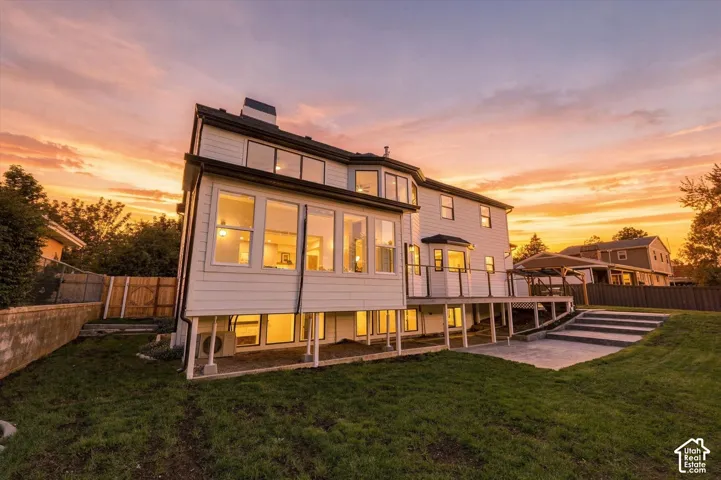 Expansive backyard featuring a manicured lawn, concrete patio with steps, and a multi-level deck with glass panel railings