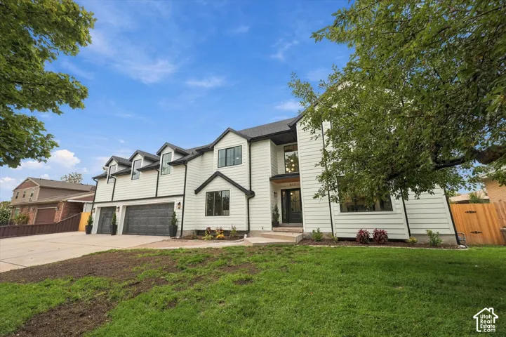Contemporary two-story exterior with white siding, black trim accents, multiple dormer windows, and a three-car garage