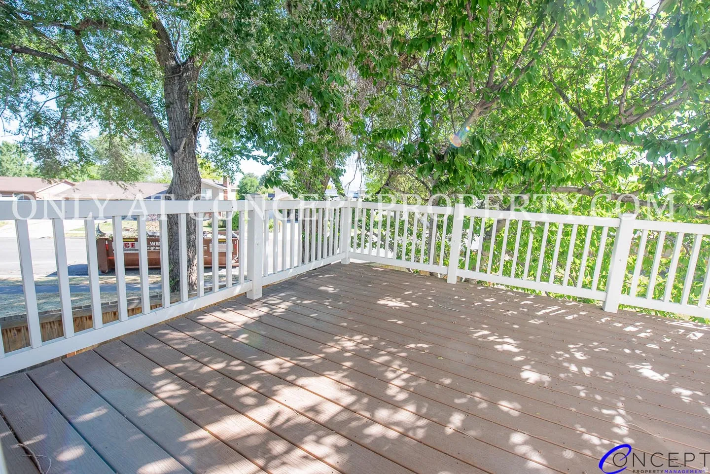 Expansive outdoor deck with wood-finish flooring and white railings, surrounded by mature trees
