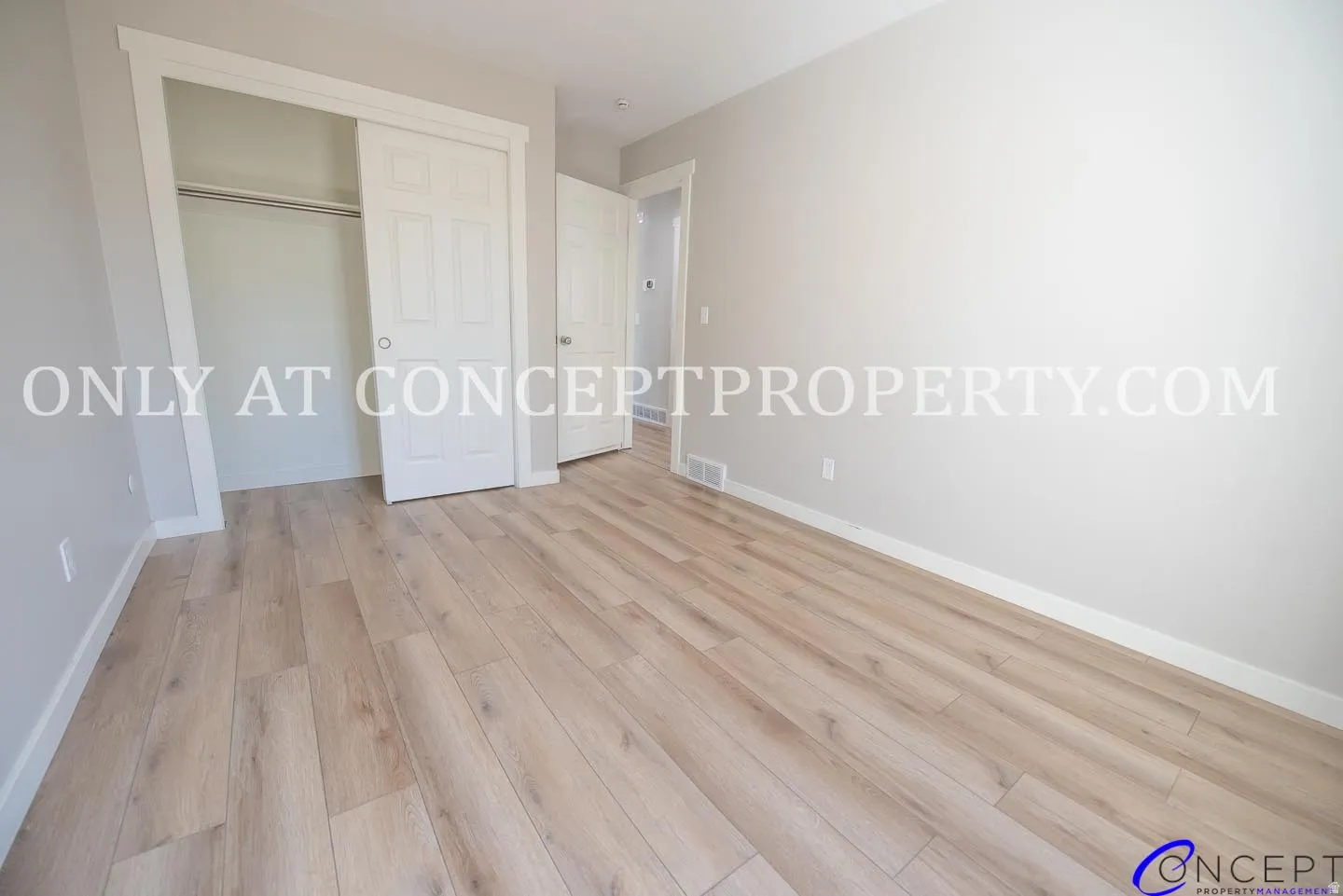 Wood-finish flooring, light grey wall paint, white trim, sliding closet doors, and recessed closet space