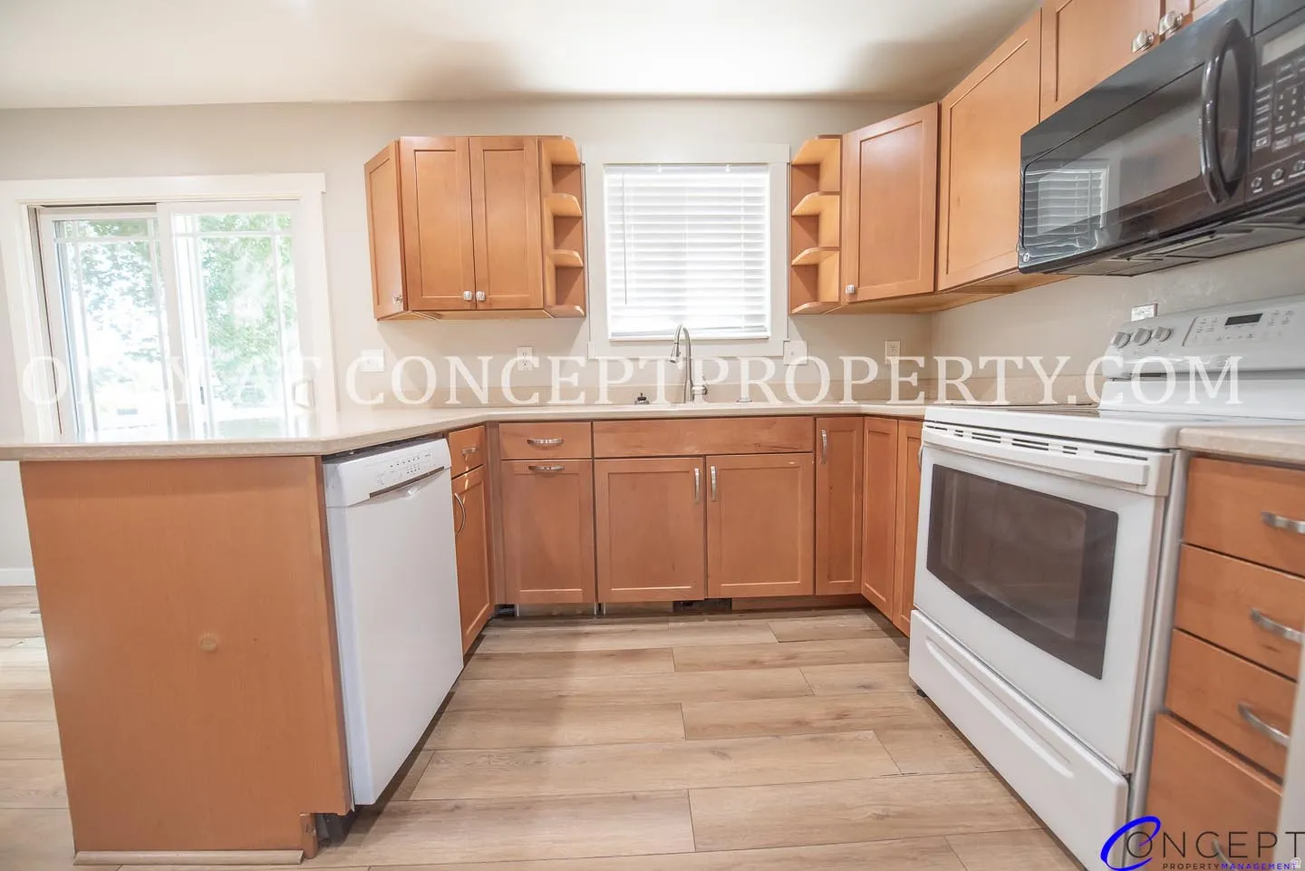 Kitchen featuring wood-finish flooring, light wood cabinetry, light-toned countertops, a stainless steel sink, and white appliances