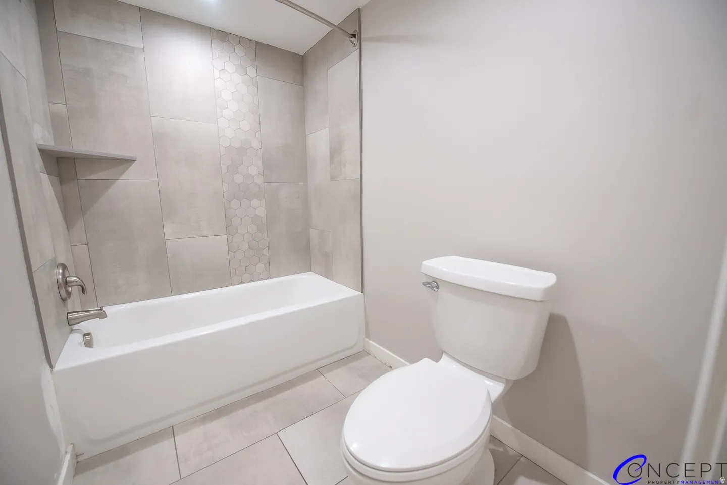 Full-size tub with brushed nickel fixtures, a tiled surround featuring a hexagonal accent stripe, and a built-in shower shelf