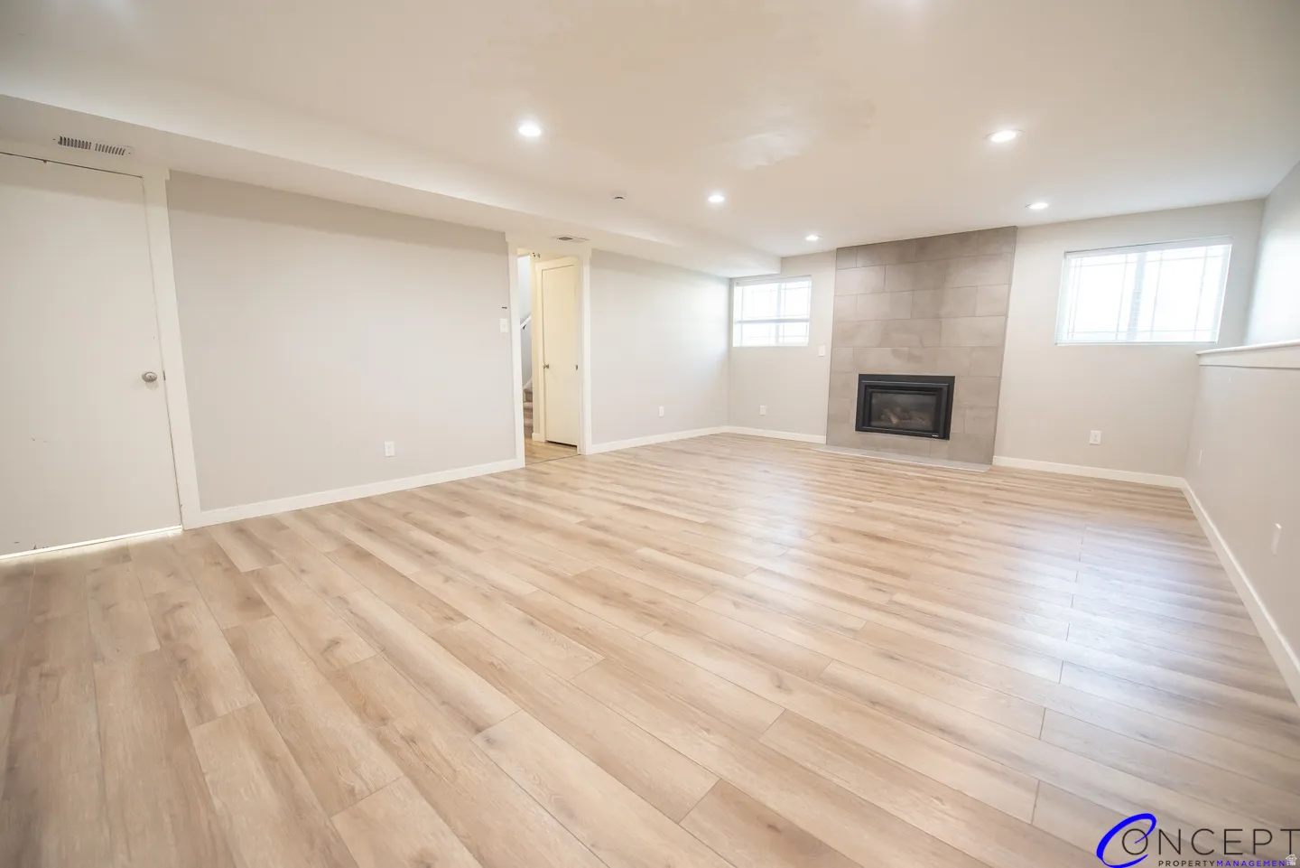 Recessed lighting illuminates the wood-finish flooring, fireplace with tile surround, and multiple windows