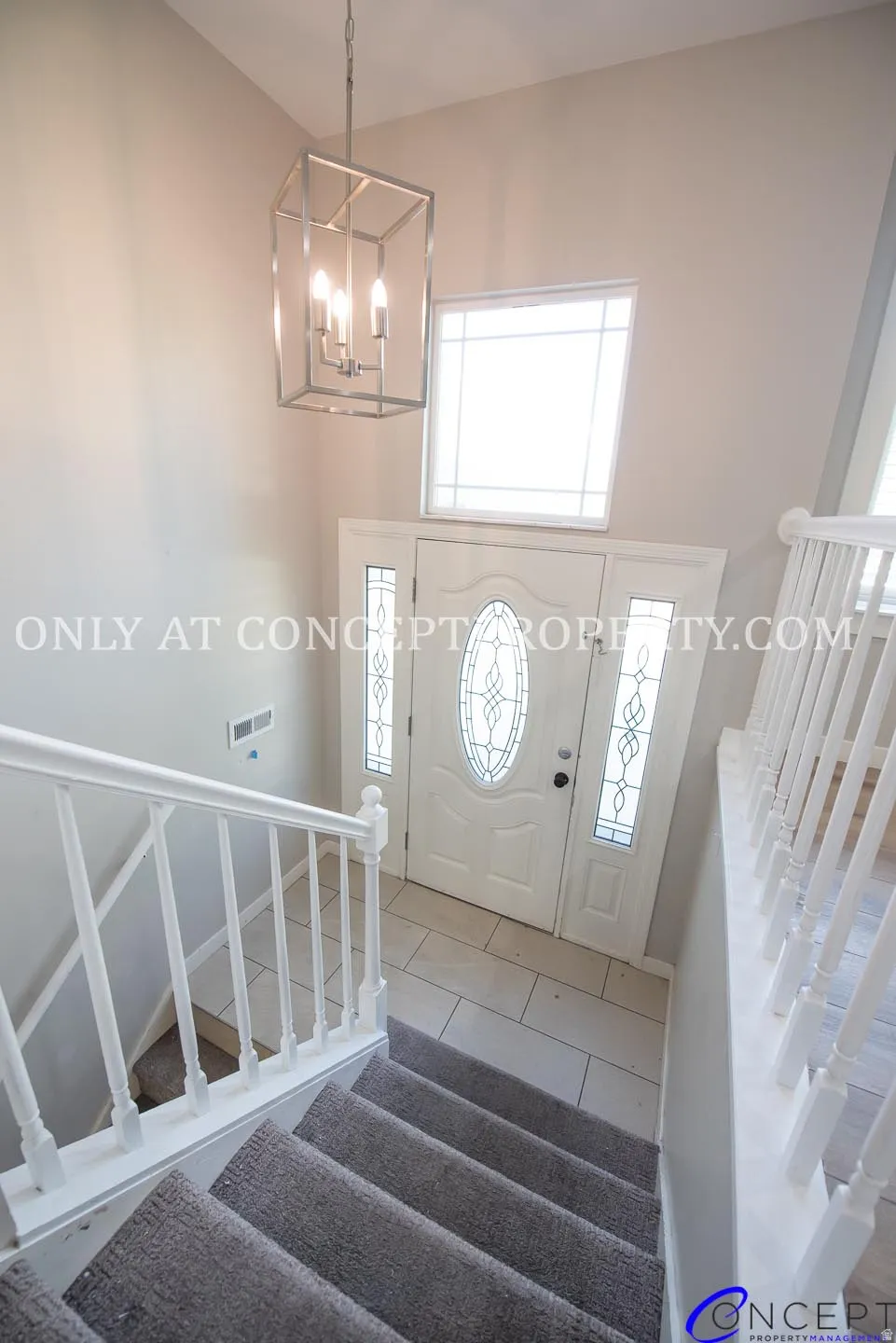 Two-story foyer with a geometric chandelier, leaded glass front door, side panel windows, tile flooring, and carpeted stairs with white balusters