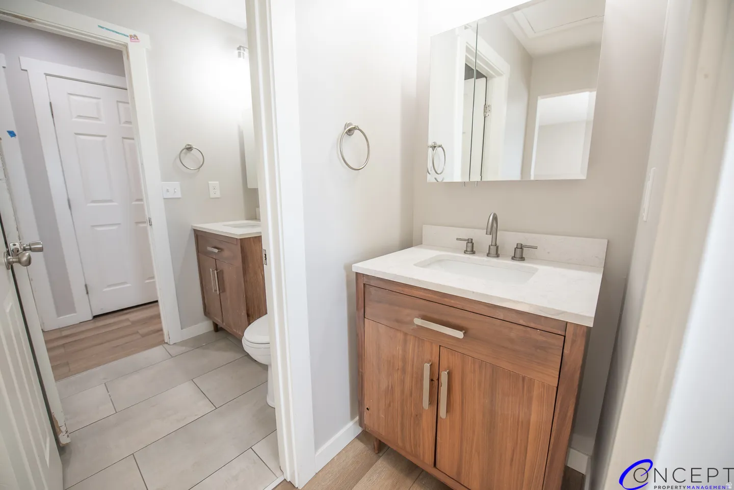 Dual wood-finish vanities with integrated sinks, framed mirrors, and light gray tile flooring