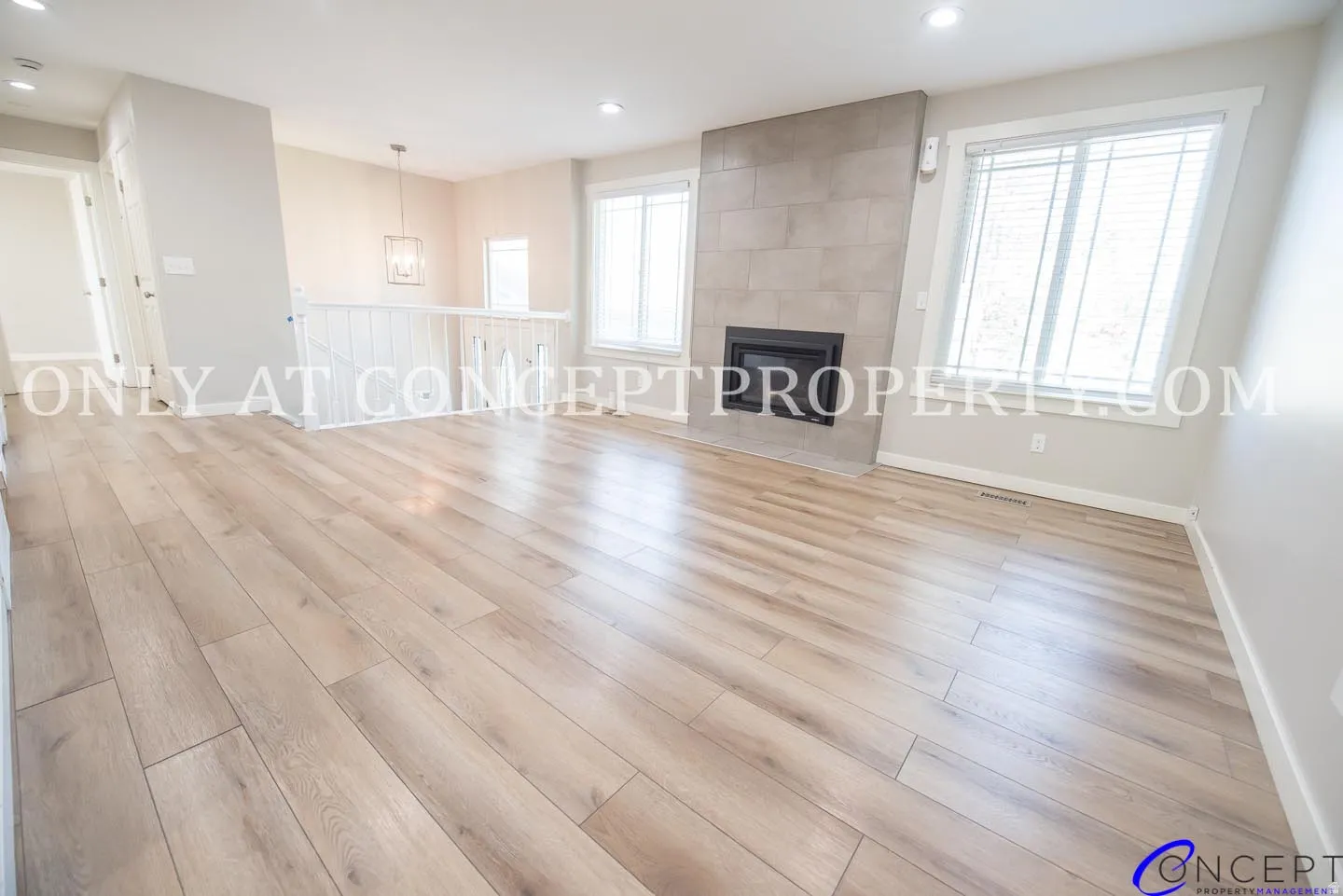 Spacious living area featuring wood-finish flooring, a tiled fireplace, and multiple windows with white trim