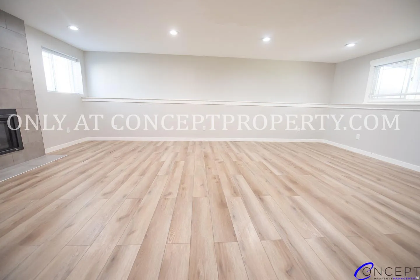Spacious room featuring wood-finish flooring, recessed lighting, a fireplace with a stone surround, and multiple windows