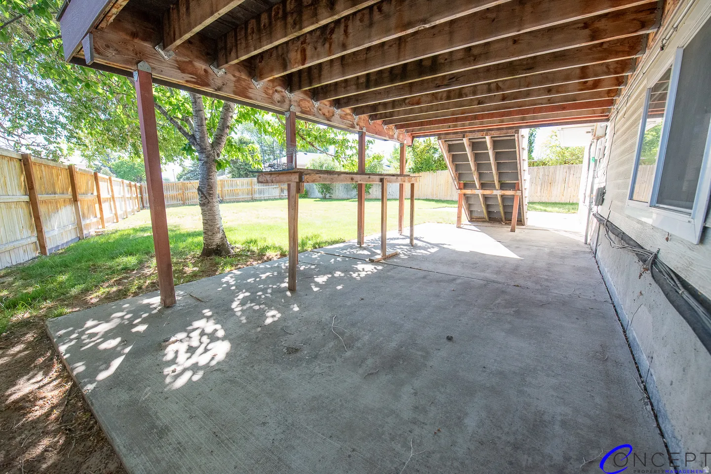 Concrete patio under a wood-beamed deck, featuring a built-in wood counter, wood privacy fence, and a grassy yard