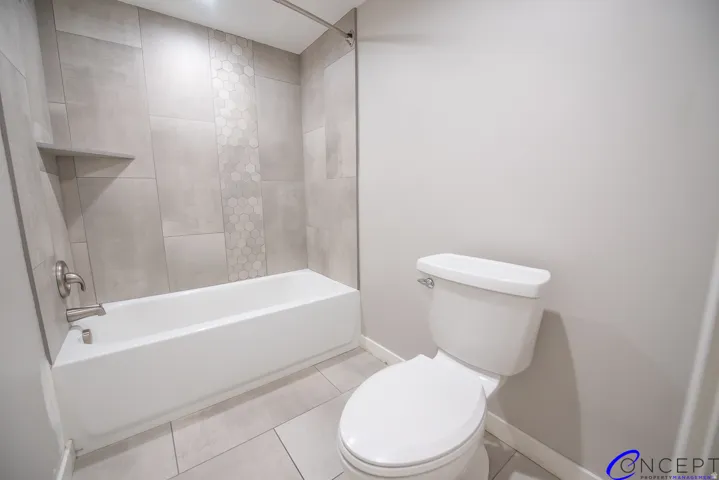 Full-size tub with brushed nickel fixtures, a tiled surround featuring a hexagonal accent stripe, and a built-in shower shelf