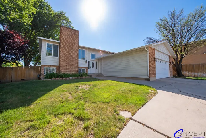 Split-level residence featuring brick and siding facade, an attached garage, a concrete driveway, and mature trees