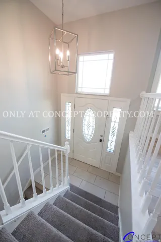 Two-story foyer with a geometric chandelier, leaded glass front door, side panel windows, tile flooring, and carpeted stairs with white balusters