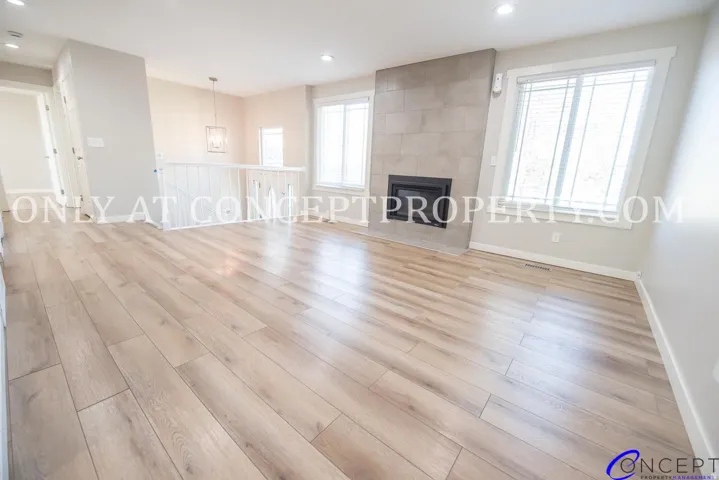 Spacious living area featuring wood-finish flooring, a tiled fireplace, and multiple windows with white trim