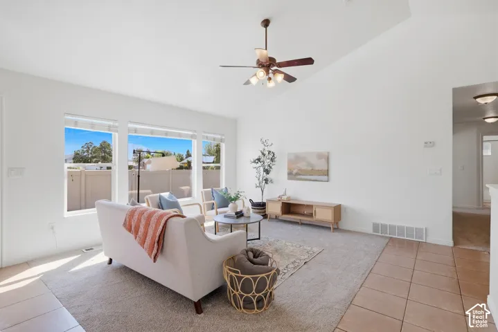 Vaulted ceiling with a ceiling fan, multiple large windows, wall-to-wall carpeting, and tile flooring