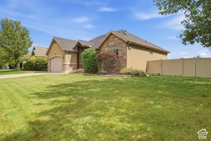 Exterior featuring stone and stucco finishes, an attached garage, a paved driveway, and a fenced backyard