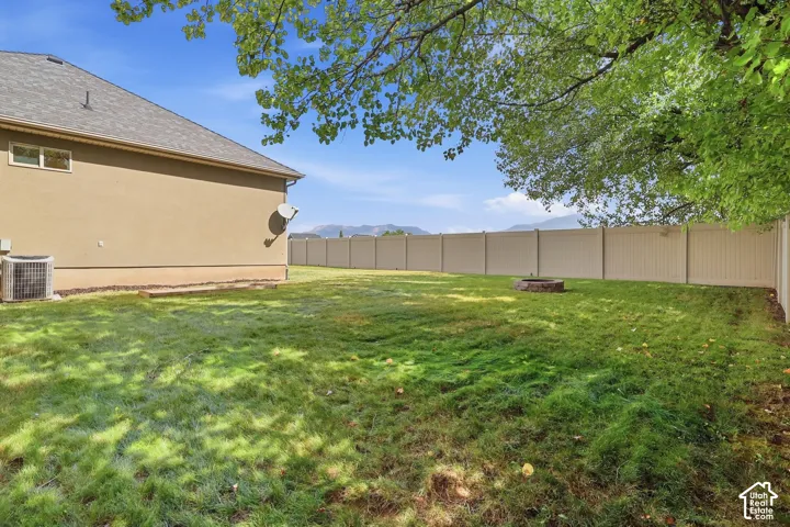 Expansive backyard featuring a privacy fence, mature trees, and mountain scenery