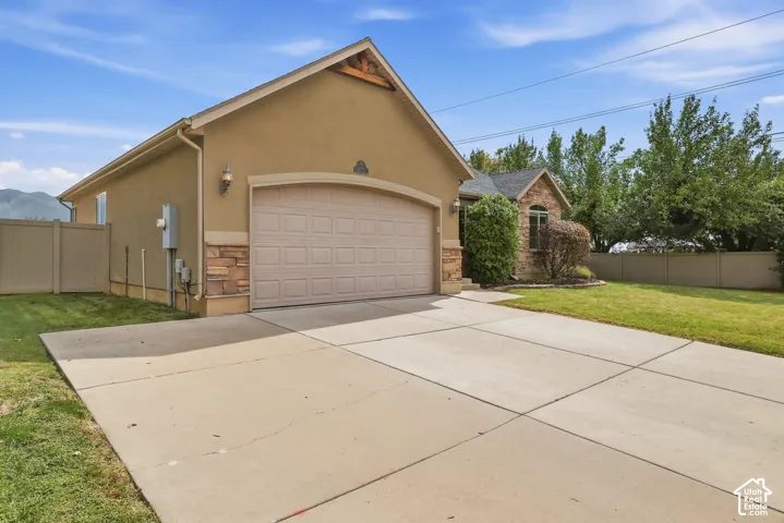 Stucco exterior with stone accents, attached garage with arched entry, concrete driveway, and established landscaping
