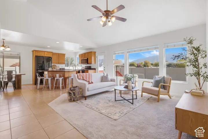 Vaulted ceiling with a ceiling fan, multiple large windows, tile flooring, wood-finish cabinetry, and a kitchen island with bar seating