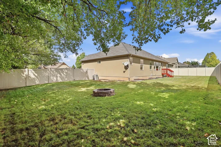 Spacious backyard featuring a grass lawn, privacy fencing, and a built-in fire pit
