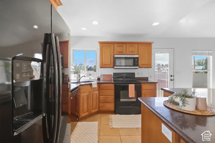 Maple cabinetry with dark countertops, tile flooring, recessed lighting, stainless steel appliances, and a glass-paneled door