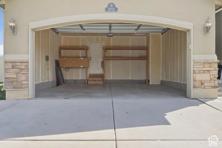 Attached two-car garage with concrete flooring, stone veneer accents, exterior wall sconces, and built-in shelving