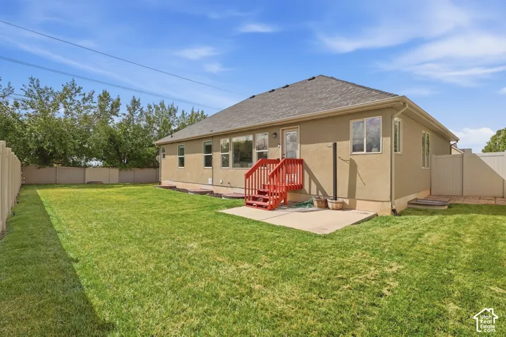 Expansive green lawn, durable stucco exterior, concrete patio, red wood-finish steps, and a privacy fence