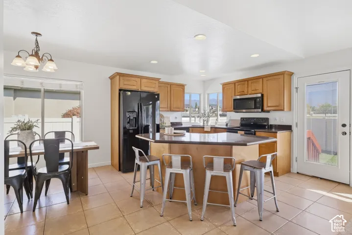 Kitchen featuring a large island with seating, wood-finish cabinetry, black appliances, and tile flooring