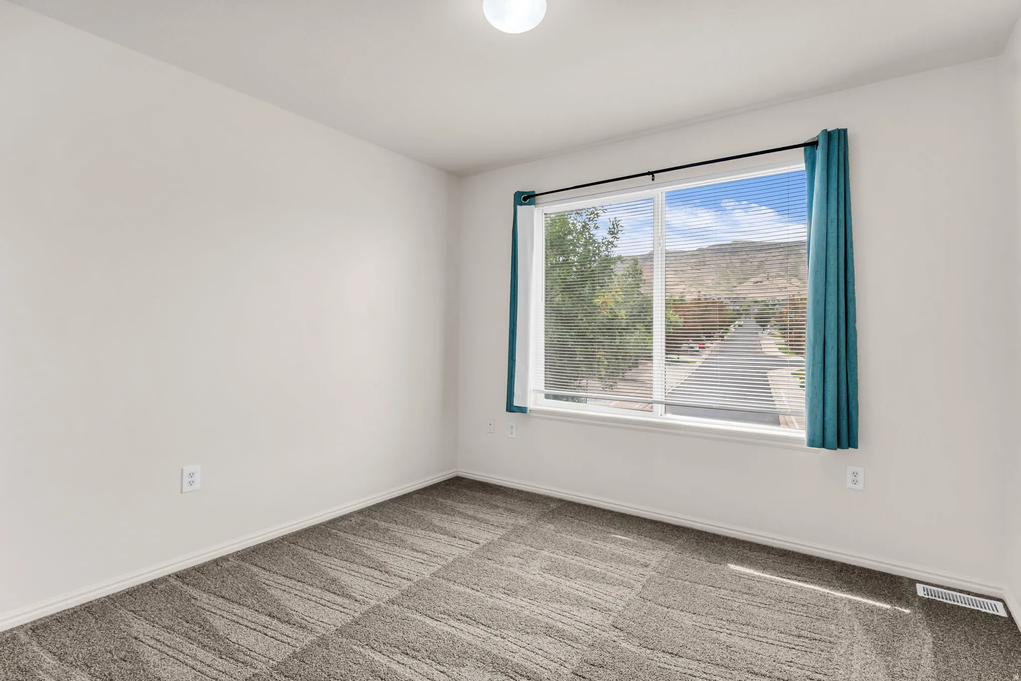 Neutral wall color, patterned carpeting, large window, and overhead lighting