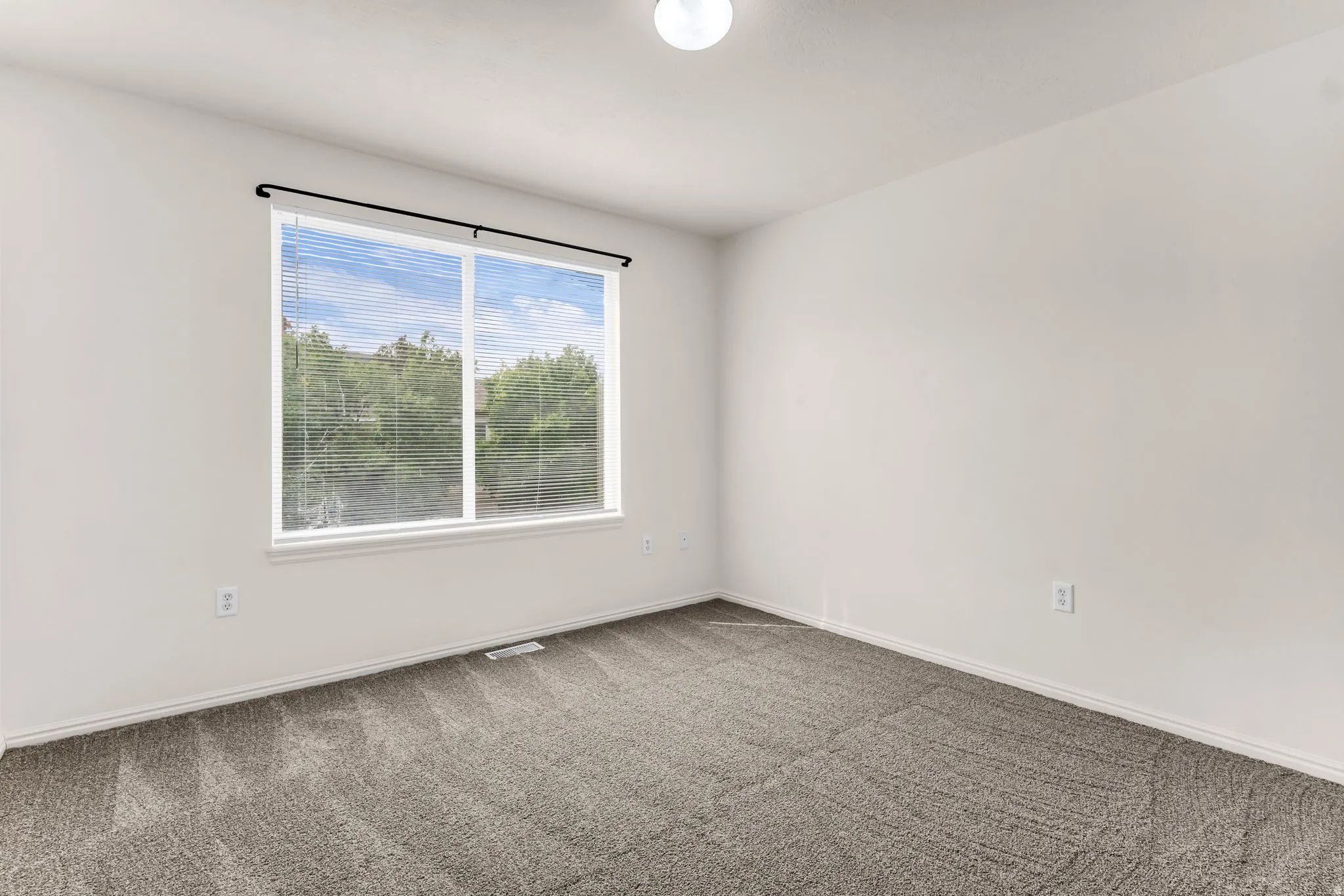 Spacious room featuring a large window, neutral wall paint, and gray patterned carpeting