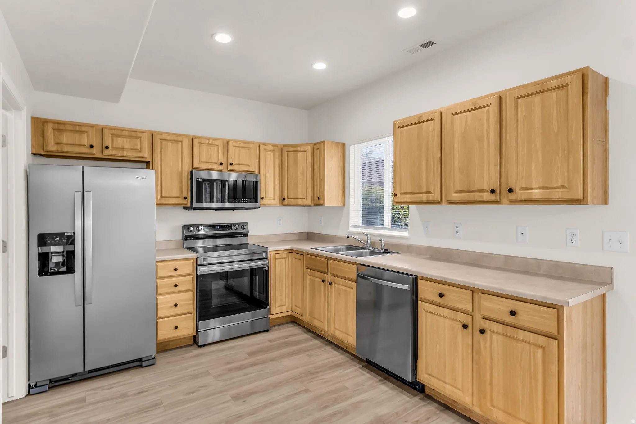 Kitchen featuring wood-finish cabinetry, stainless steel appliances, light-toned countertops, and wood-look flooring