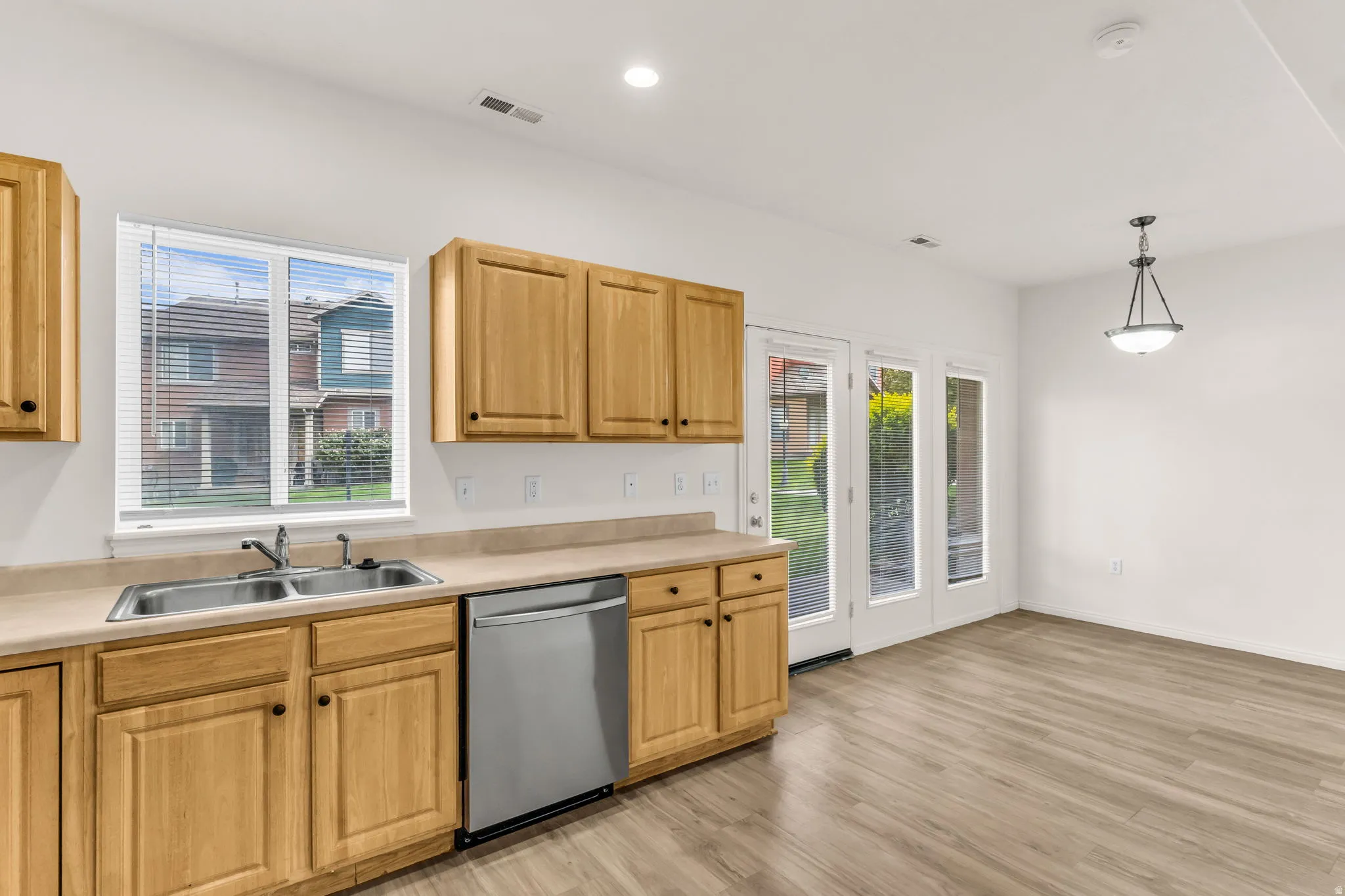 Wood-finish flooring throughout, light wood cabinetry, stainless steel dishwasher, double basin sink, and dual glass-paned doors