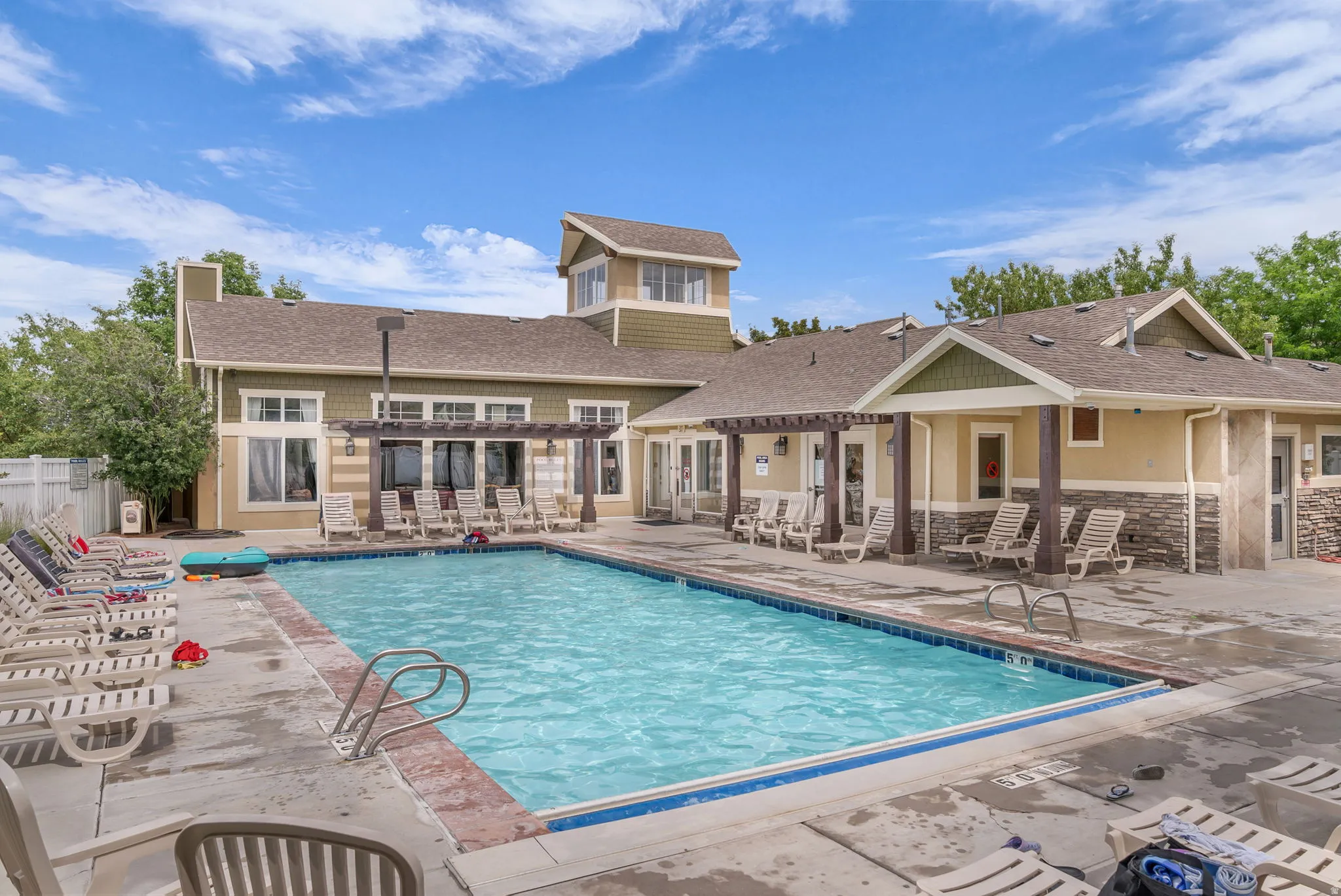 Outdoor swimming pool with concrete decking, pergola-covered patio, and a building featuring stone veneer accents