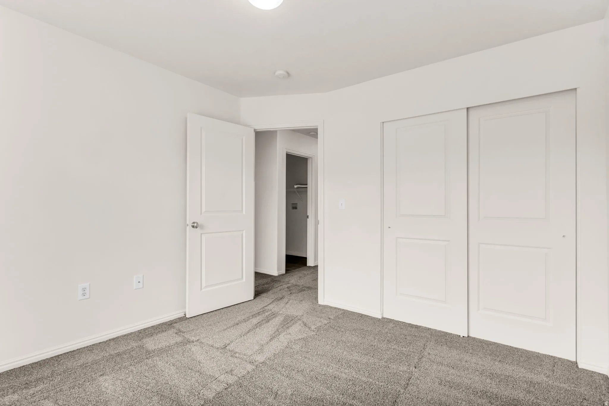 Gray carpeting with white trim and white walls, featuring a white door with a polished chrome handle and white sliding closet doors