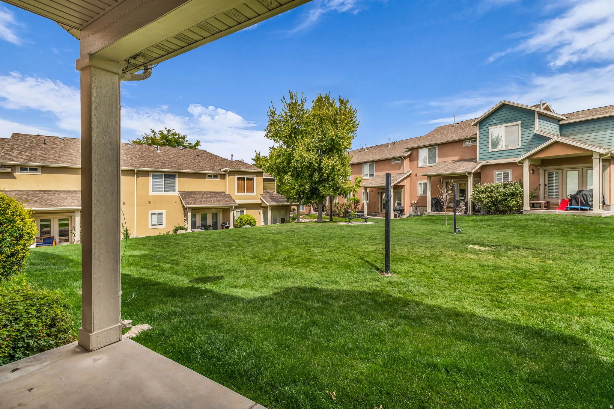 Expansive green space with mature trees and multiple stucco townhomes featuring patios and balconies