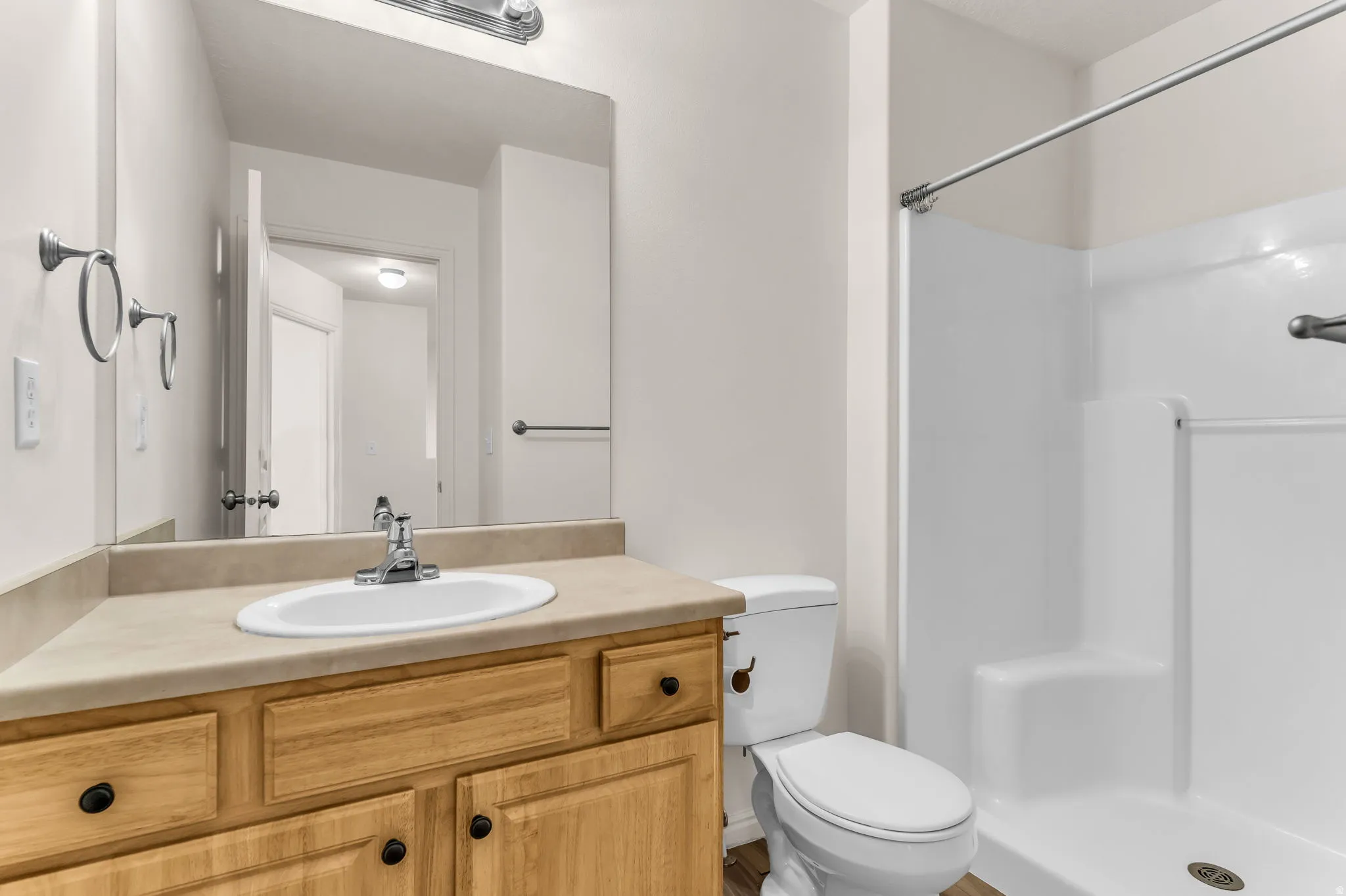 Bathroom featuring a wood-finish vanity with a laminate countertop, an undermount sink, and a white shower stall
