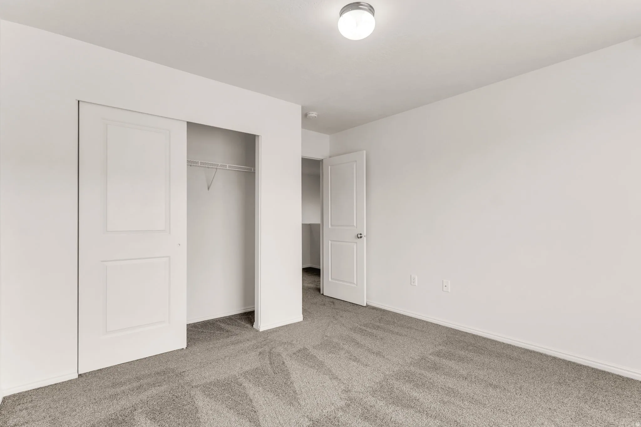 Neutral tone walls, grey patterned carpeting, white interior doors, and a built-in closet with sliding doors