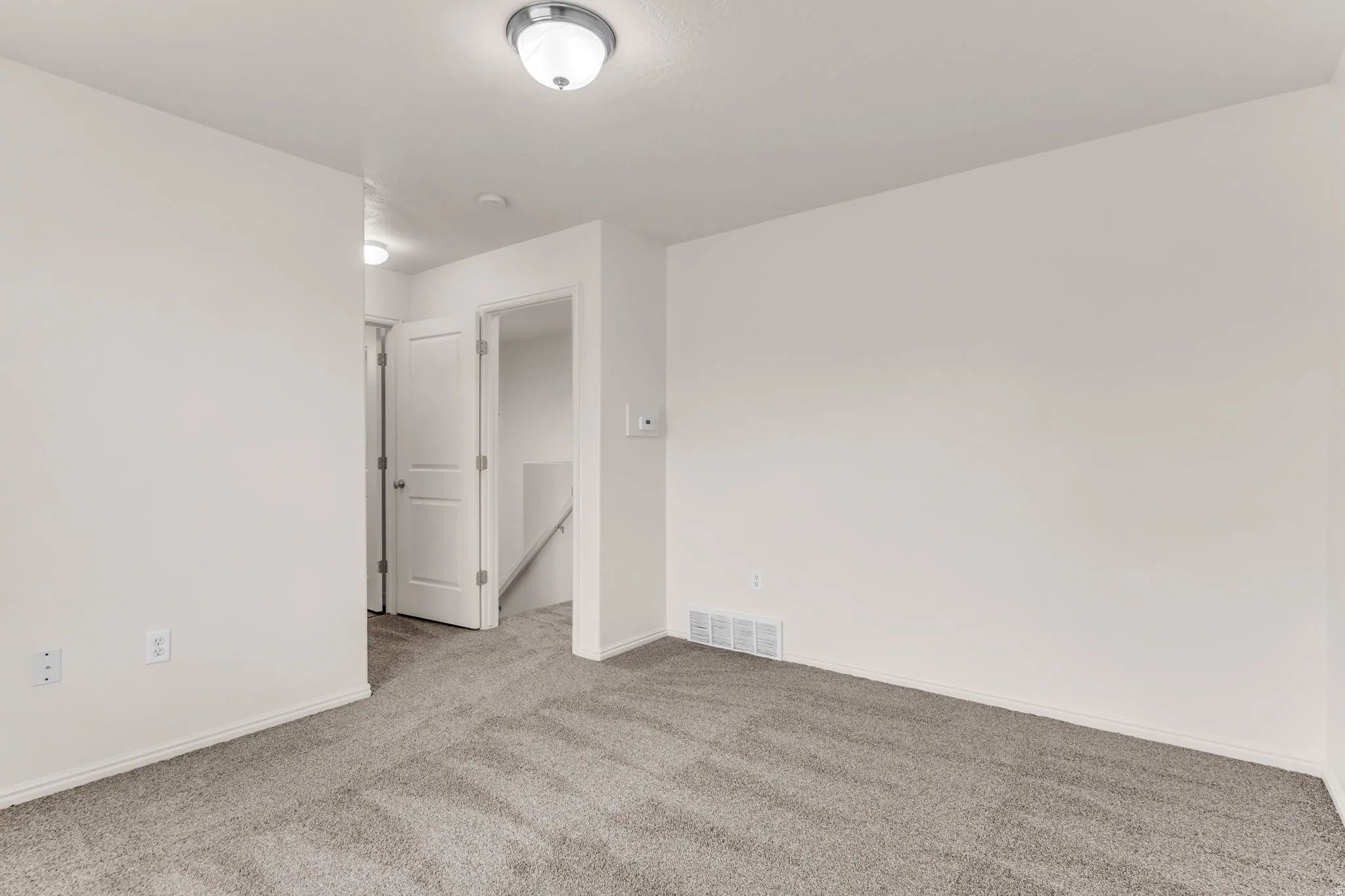 Neutral-toned carpeting, white walls, and a contemporary flush-mount ceiling light