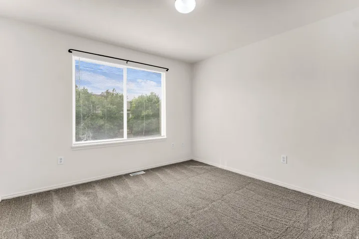 Spacious room featuring a large window, neutral wall paint, and gray patterned carpeting