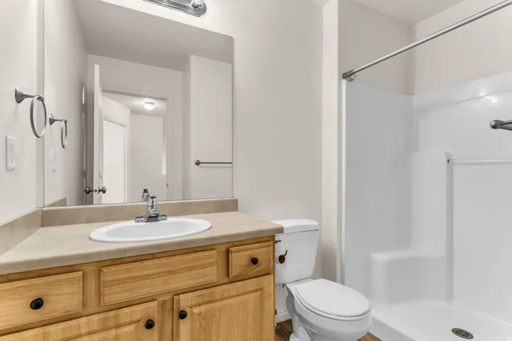 Bathroom featuring a wood-finish vanity with a laminate countertop, an undermount sink, and a white shower stall