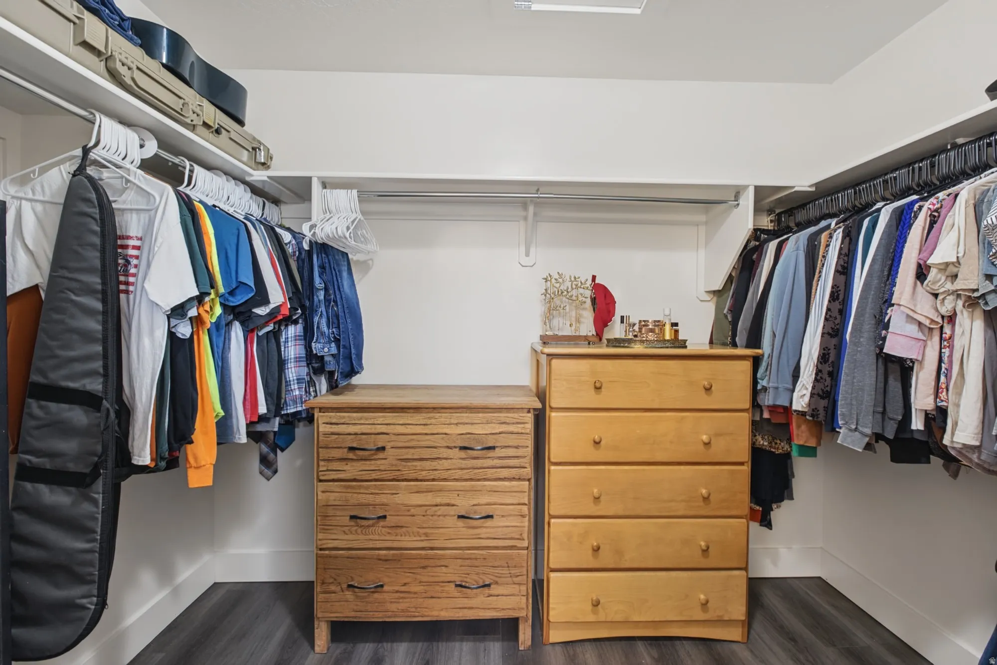 Custom closet system with white shelving, multiple hanging rods, and dark wood-finish flooring