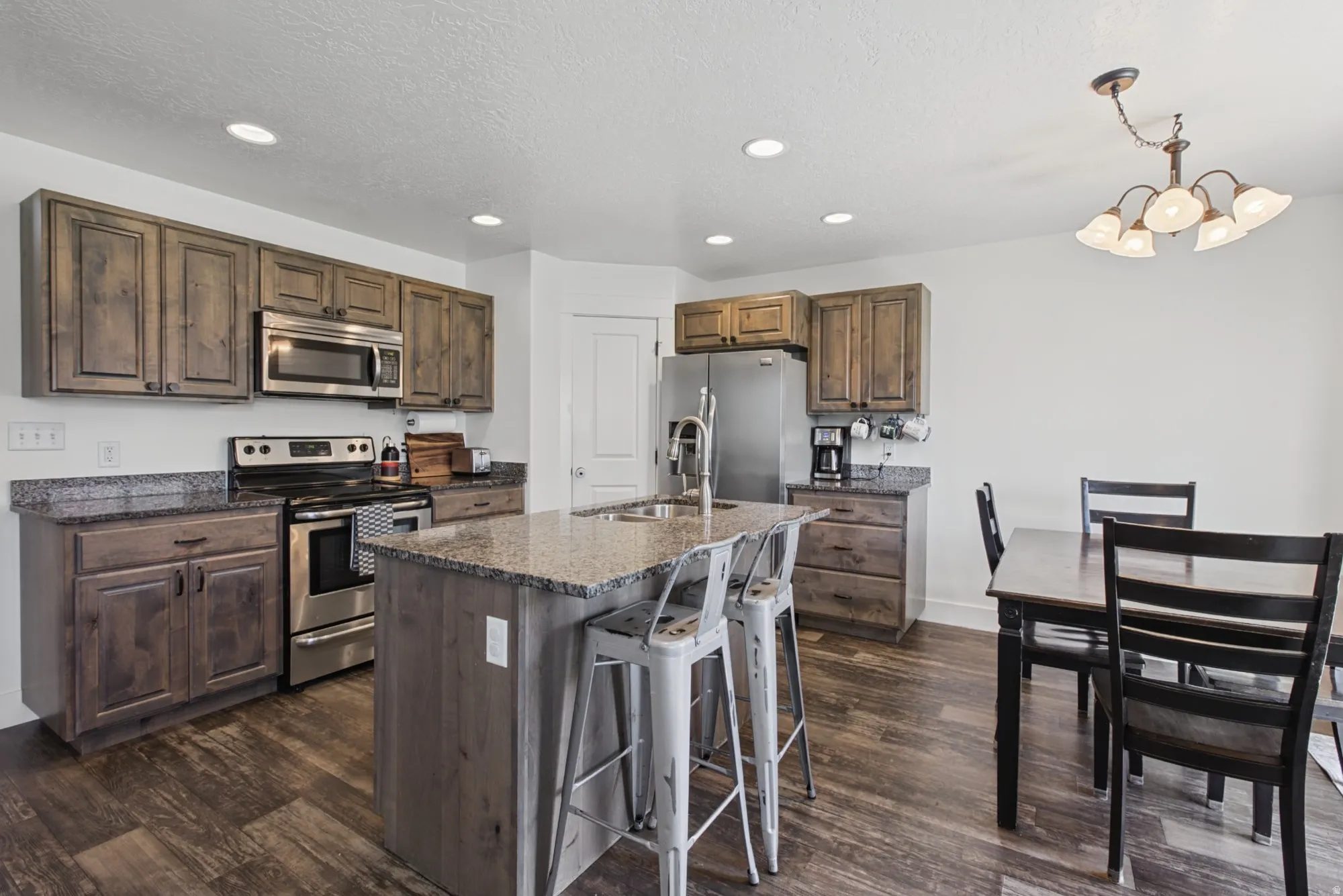 Kitchen featuring wood-finish cabinetry, granite countertops, stainless steel appliances, a center island with sink, and wood-finish flooring