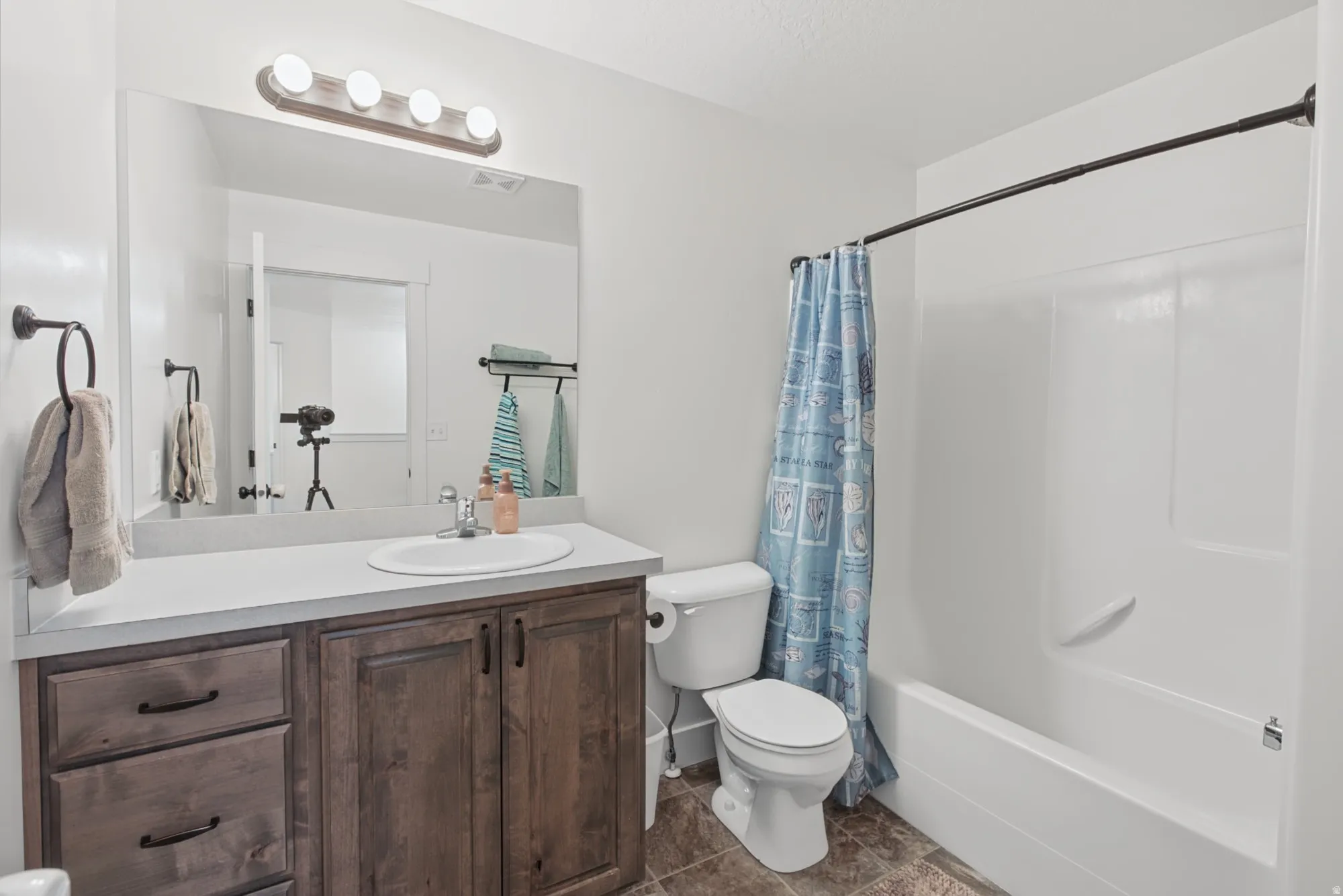 Bathroom featuring a wood-finish vanity with a white countertop, an undermount sink, a large mirror, and a shower-over-tub combination
