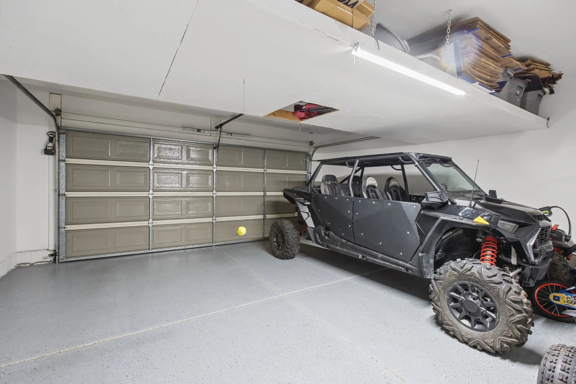 Garage featuring a panel-style door, finished flooring, built-in overhead storage, and fluorescent lighting