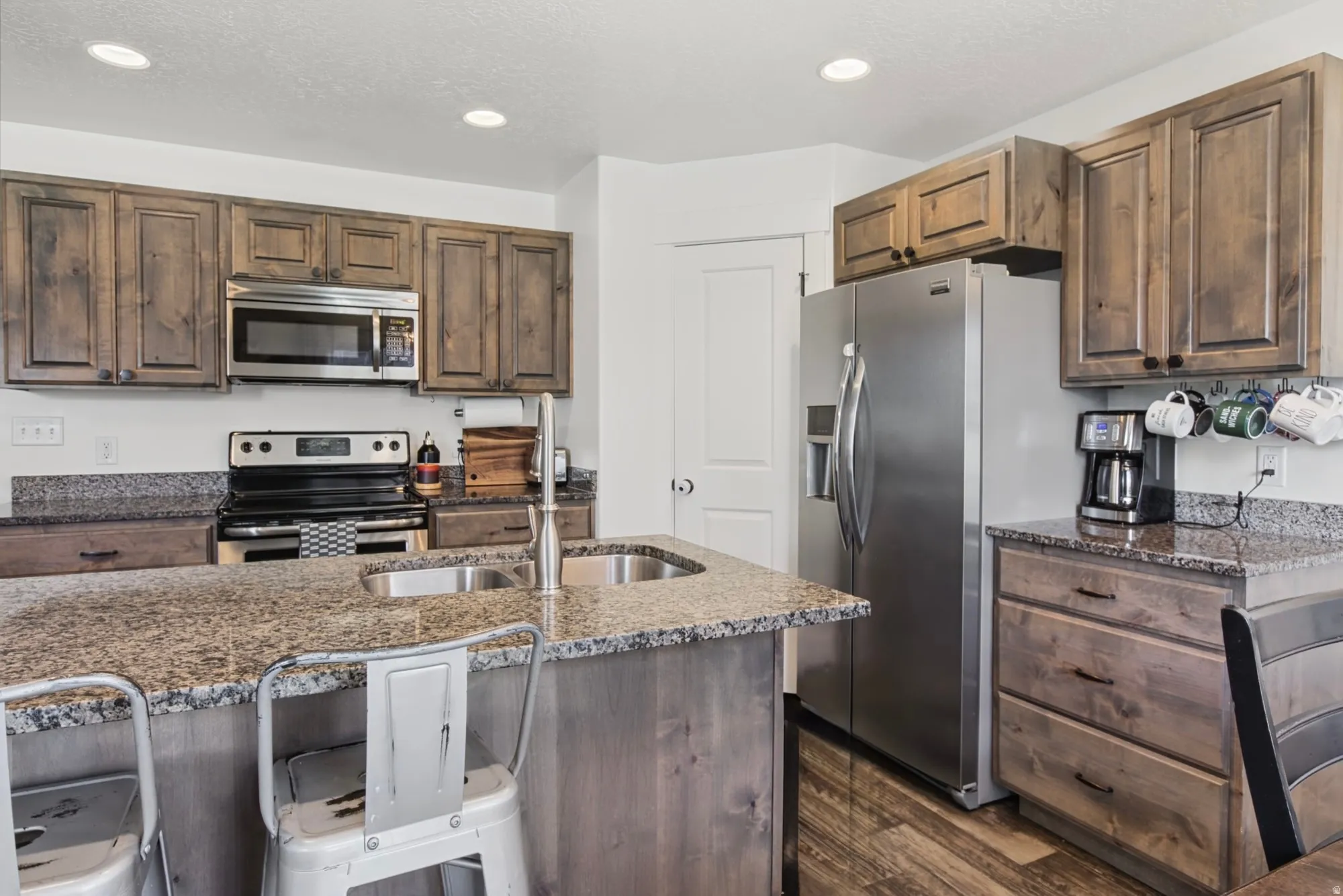 Kitchen featuring wood-finish cabinetry, stainless steel appliances, granite countertops, and an integrated kitchen island with a double basin sink