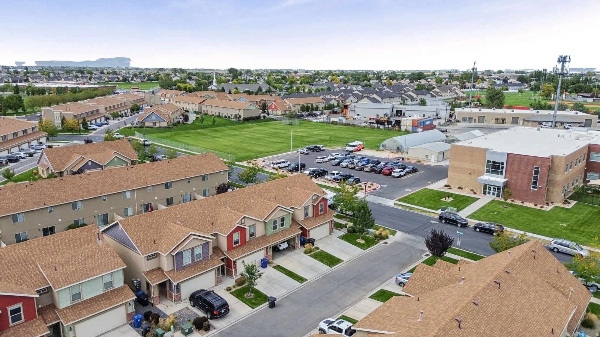 Residential community with townhomes and detached properties, featuring a large grassy common area and adjacent commercial structures