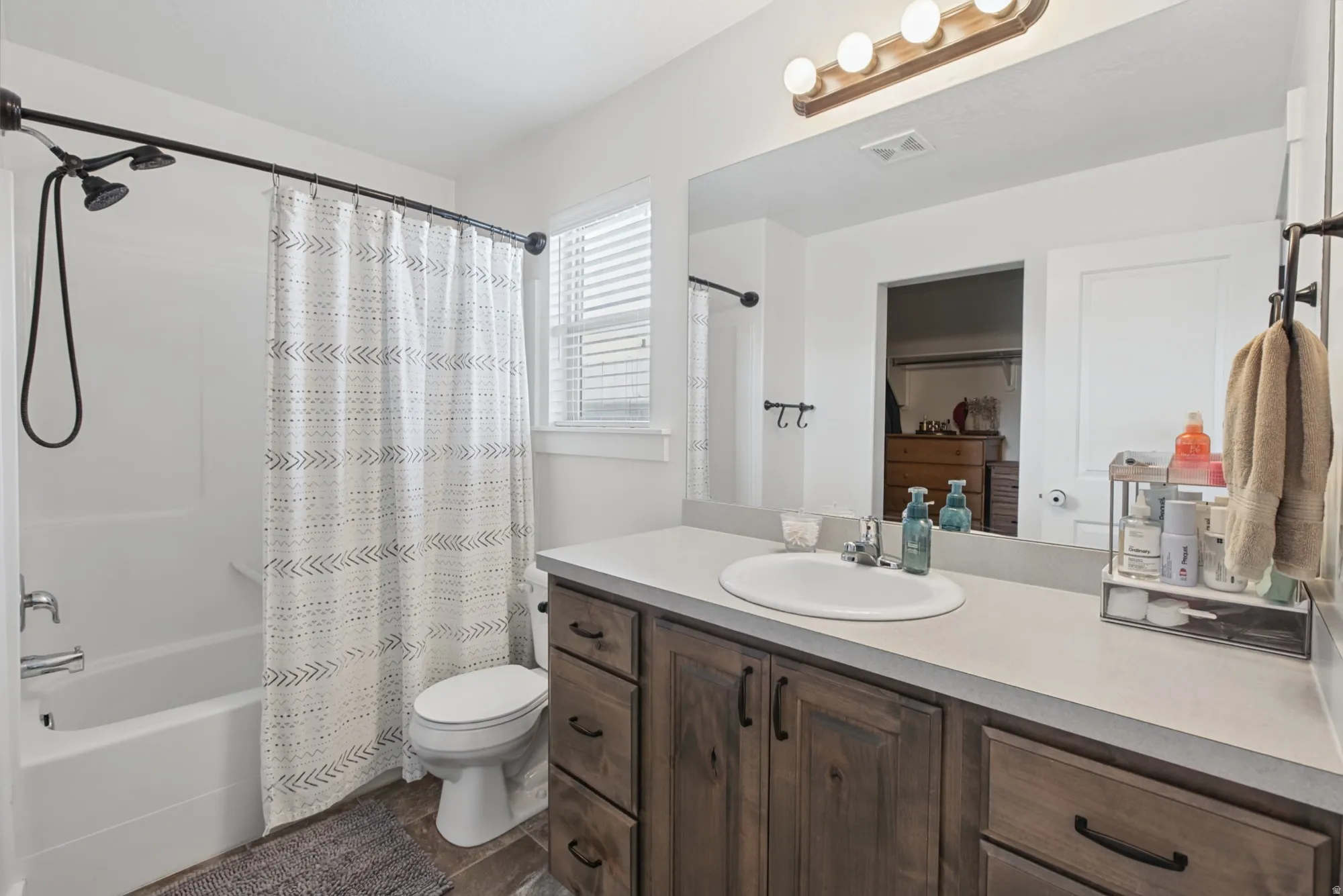 Bathroom featuring a wood-finish vanity with a light-toned countertop, an integrated sink, a large wall-mounted mirror, and a tub/shower combination with a multi-function showerhead