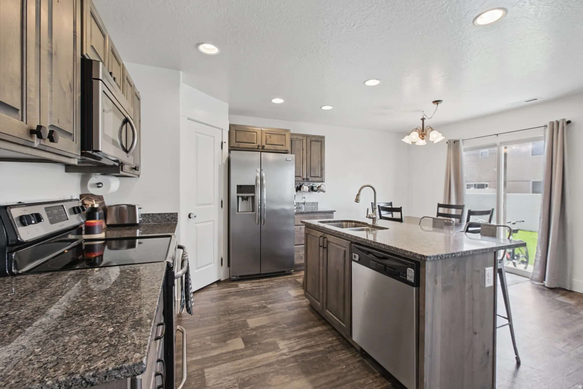 Kitchen featuring wood-finish cabinetry, stainless steel appliances, speckled countertops, and recessed lighting
