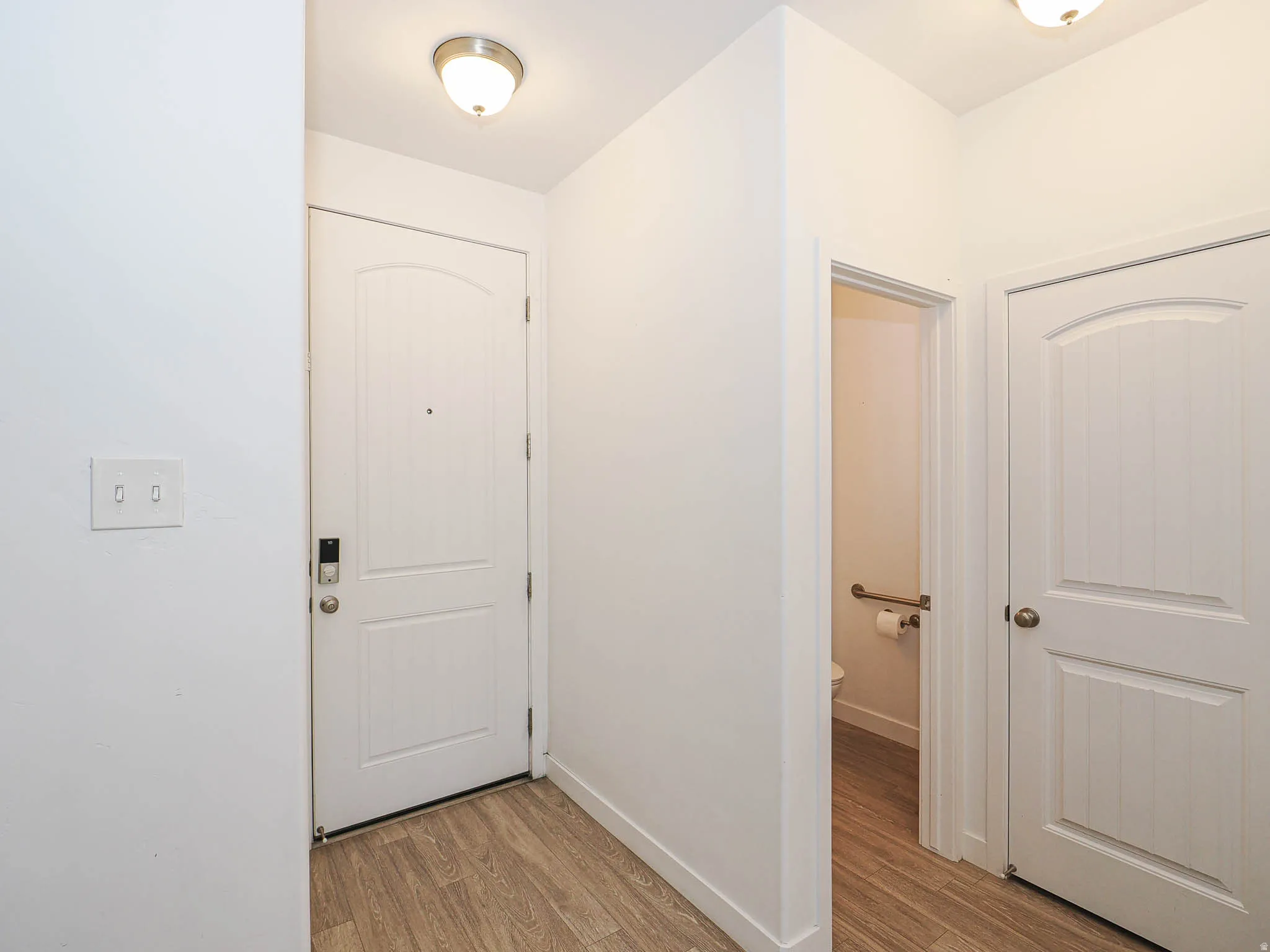Wood-finish flooring, white paneled doors, and ceiling-mounted light fixtures