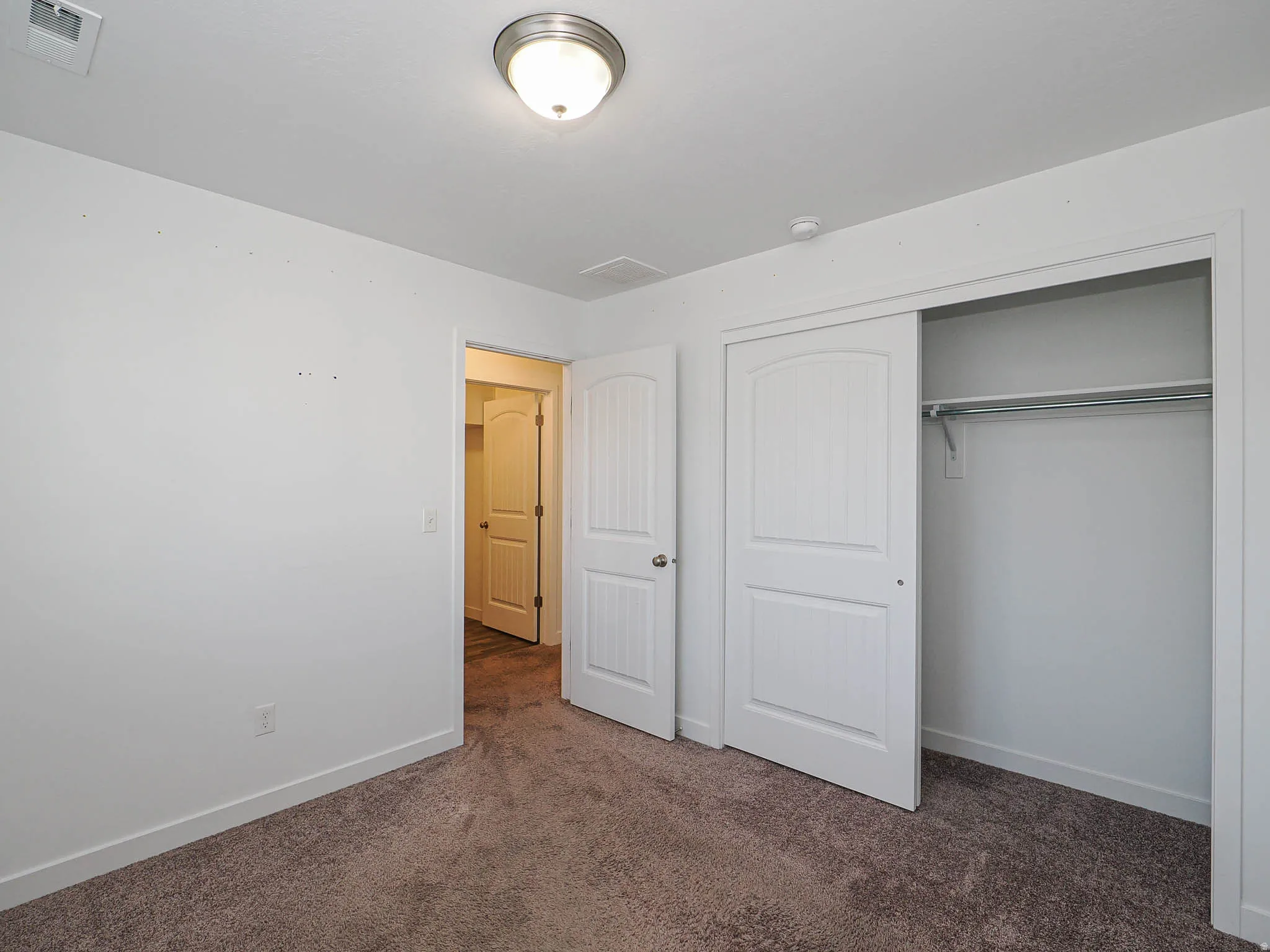 Plush carpet flooring, ceiling-mounted light fixture, white interior doors, and a double-door closet with a hanging rod