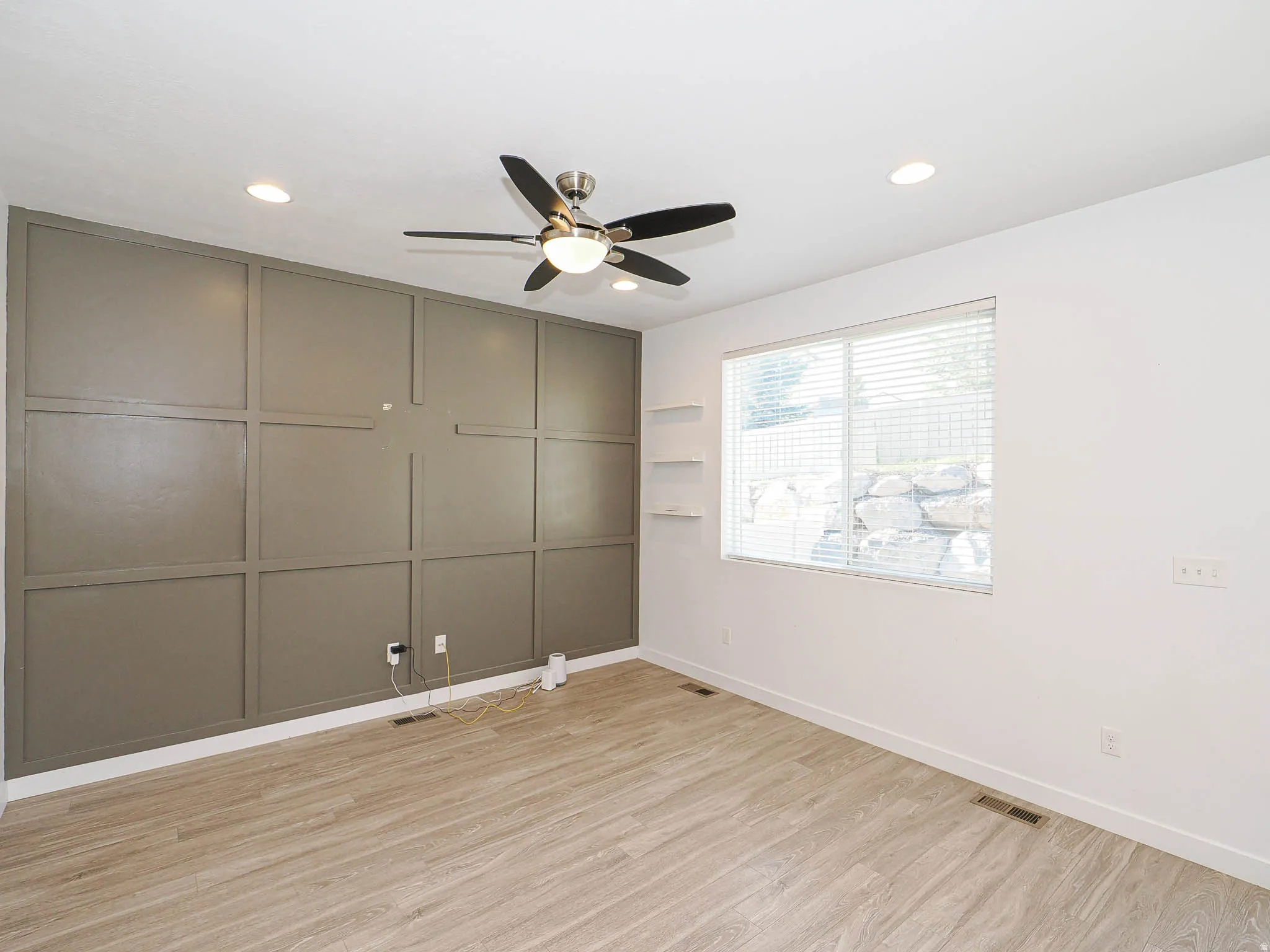 Accent wall with decorative paneling, wood-finish flooring, ceiling fan with light, recessed lighting, and built-in shelving
